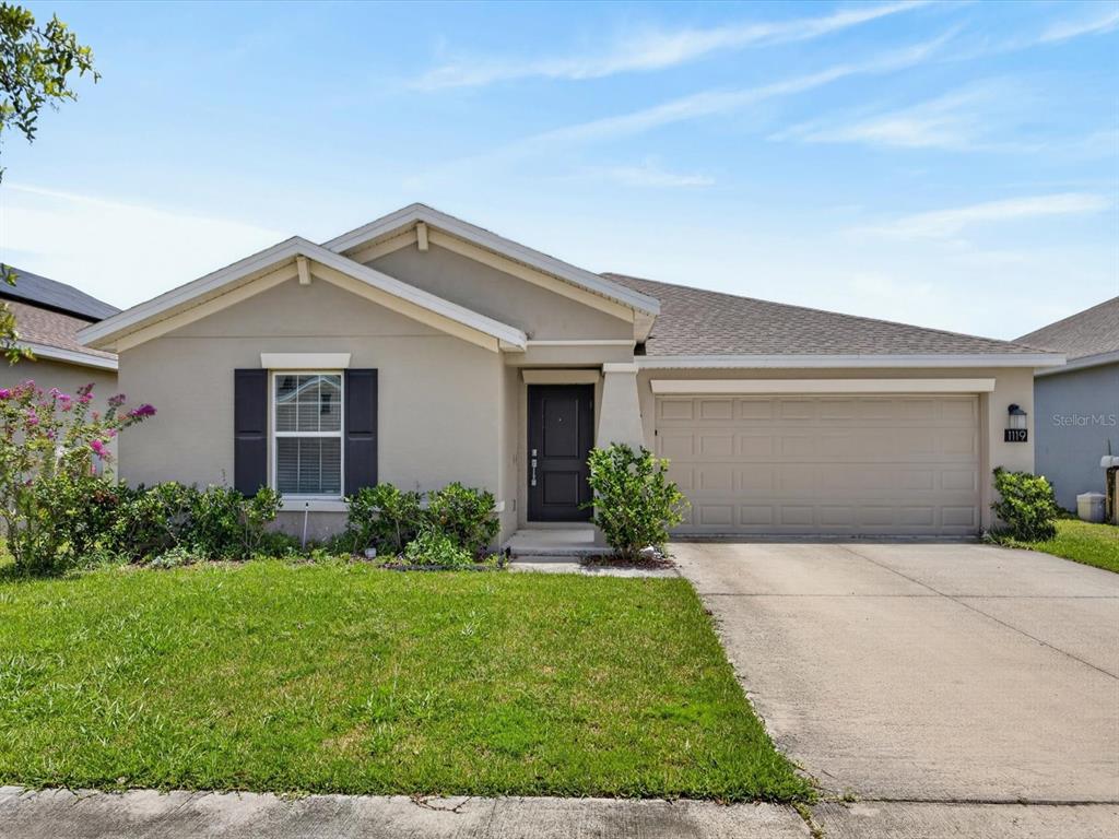 A single-story suburban house with a beige stucco exterior, a two-car garage, and a lawn — 1119 JAMES PAUL ROAD, DAVENPORT, FL