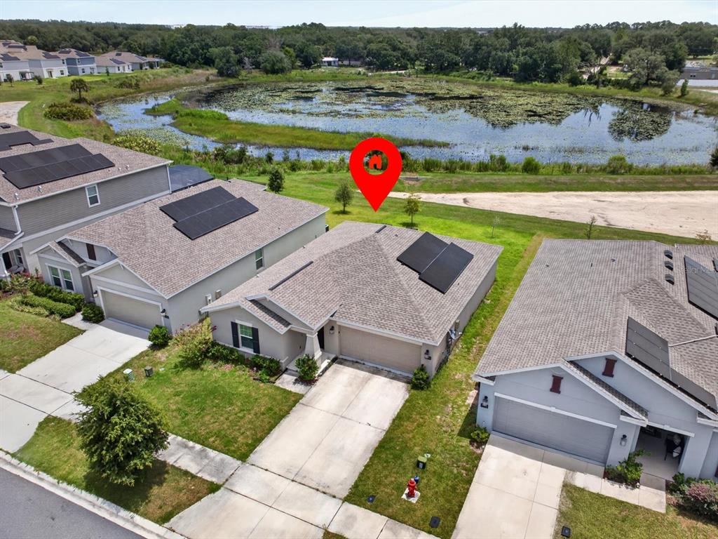 An aerial view shows a suburban house with solar panels overlooking a pond — 1119 JAMES PAUL ROAD, DAVENPORT, FL