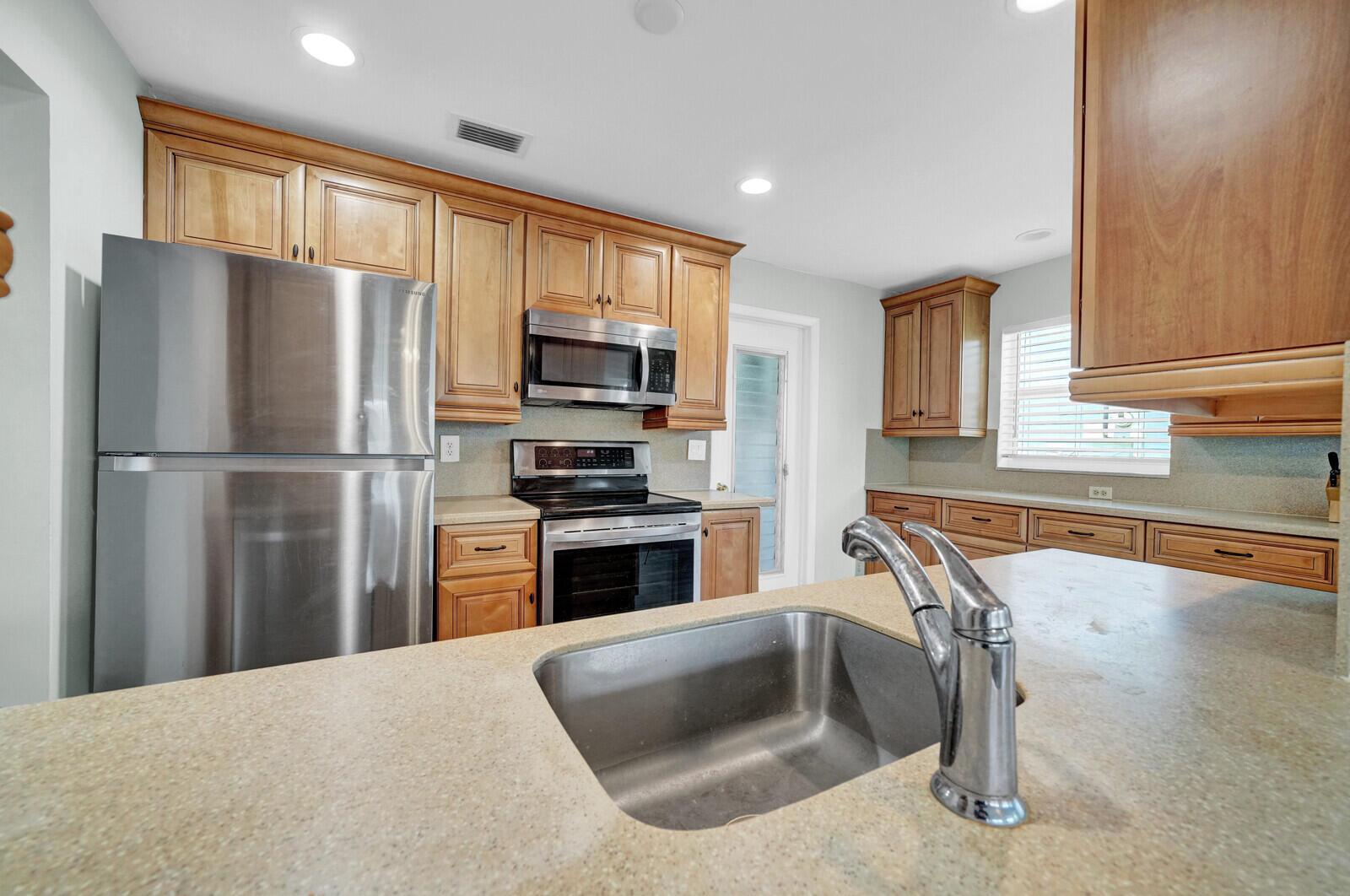 A kitchen features wood cabinets, stainless steel appliances, a sink island, and light-colored countertops — 714 SW 16th Street, Boynton Beach FL 33426, BOYNTON BEACH, FL