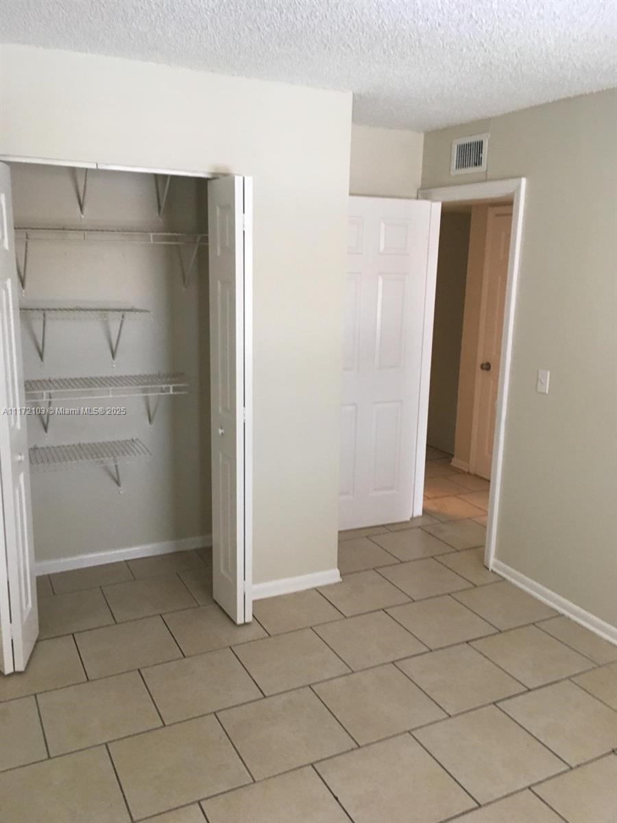 This room features beige tile flooring, a white bi-fold closet with wire shelving, and a doorway — 5962 NW 29th Pl # 112, Sunrise FL 33313, SUNRISE, FL