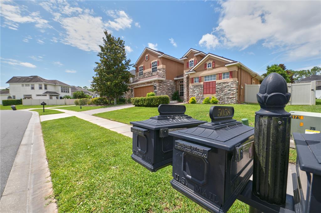 A two-story suburban house with stone veneer and a multi-car garage behind several mailboxes — 5058 OTTERS DEN TRAIL, SANFORD, FL