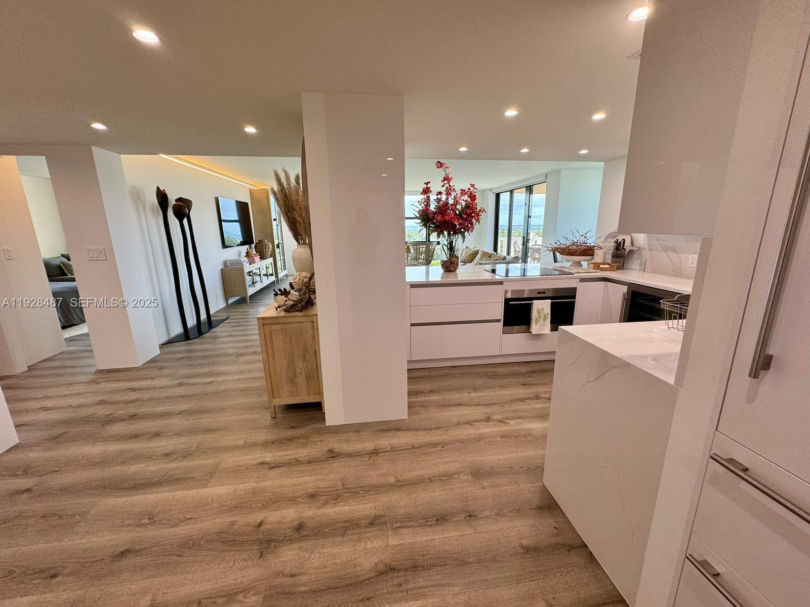 A modern kitchen features white cabinetry, marble-style countertops, and light wood-look flooring — 1121 Crandon Blvd # E1001, Key Biscayne FL 33149, KEY BISCAYNE, FL
