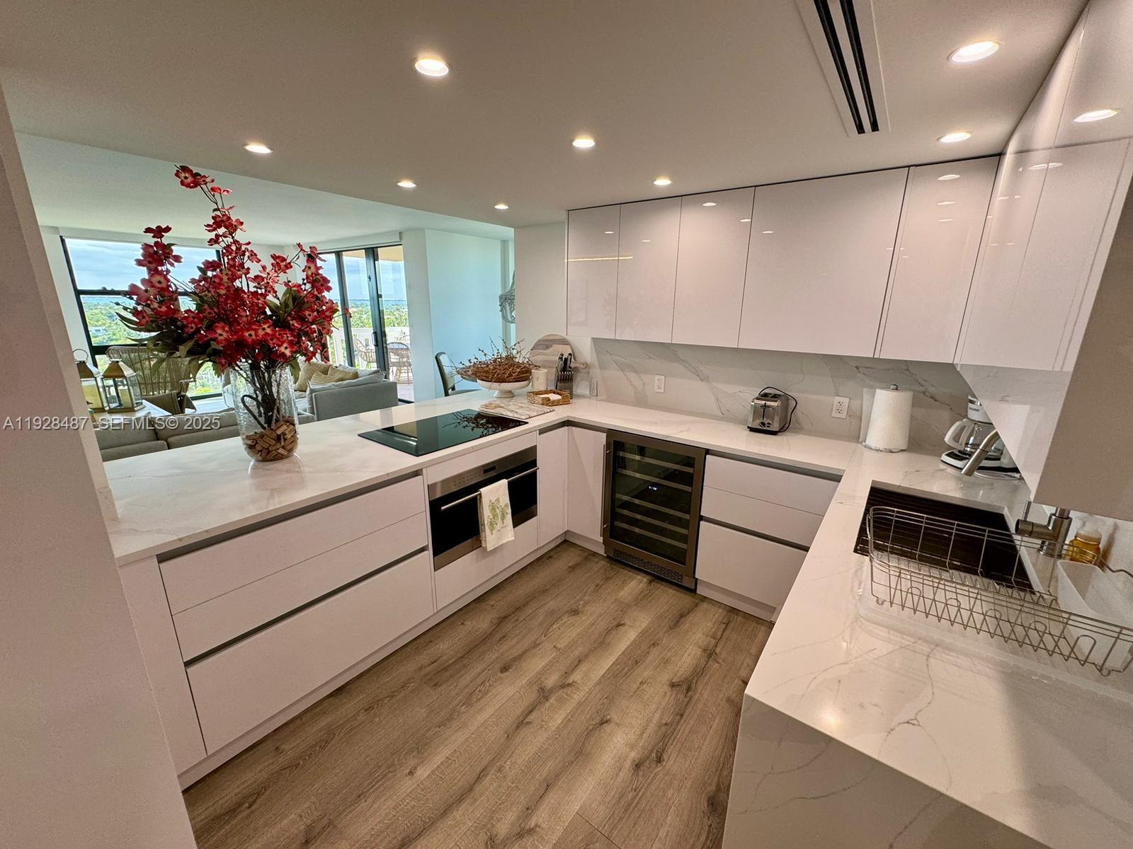 A modern kitchen features white cabinets, quartz countertops, a wine cooler, and wood-look flooring — 1121 Crandon Blvd # E1001, Key Biscayne FL 33149, KEY BISCAYNE, FL
