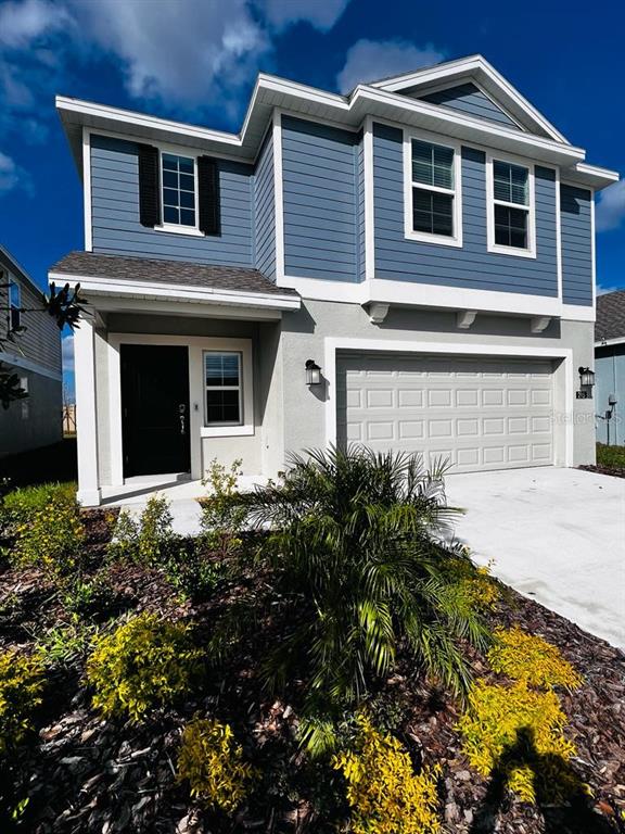A two-story house with blue horizontal siding, a gray garage door, and a front garden — 215 AQUA AVENUE, DAVENPORT, FL