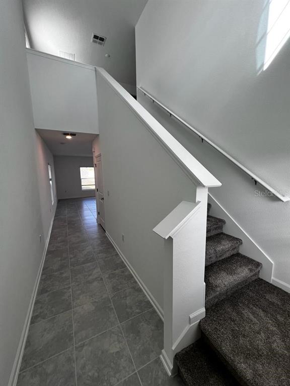 A hallway with tile flooring leads to a staircase with carpeted steps and a handrail — 215 AQUA AVENUE, DAVENPORT, FL