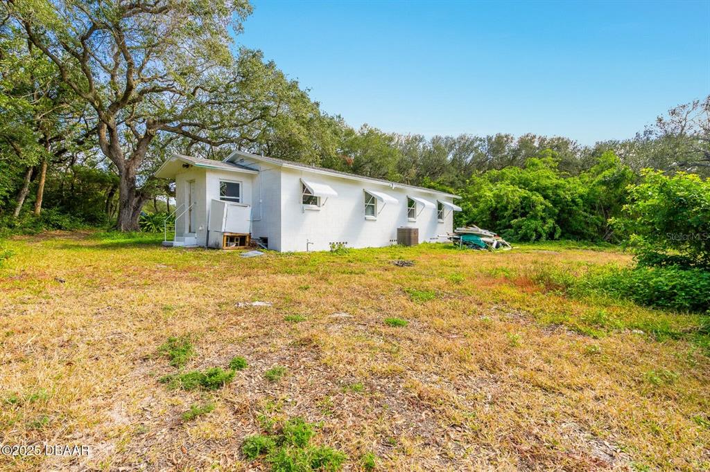 A white, single-story house sits on a grassy lot surrounded by trees and vegetation — 4770 S PENINSULA DRIVE, PONCE INLET, FL