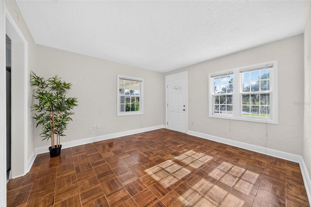 An empty room with parquet wood flooring, white walls, a front door, and two windows — 1333 S DENNING DRIVE, WINTER PARK, FL