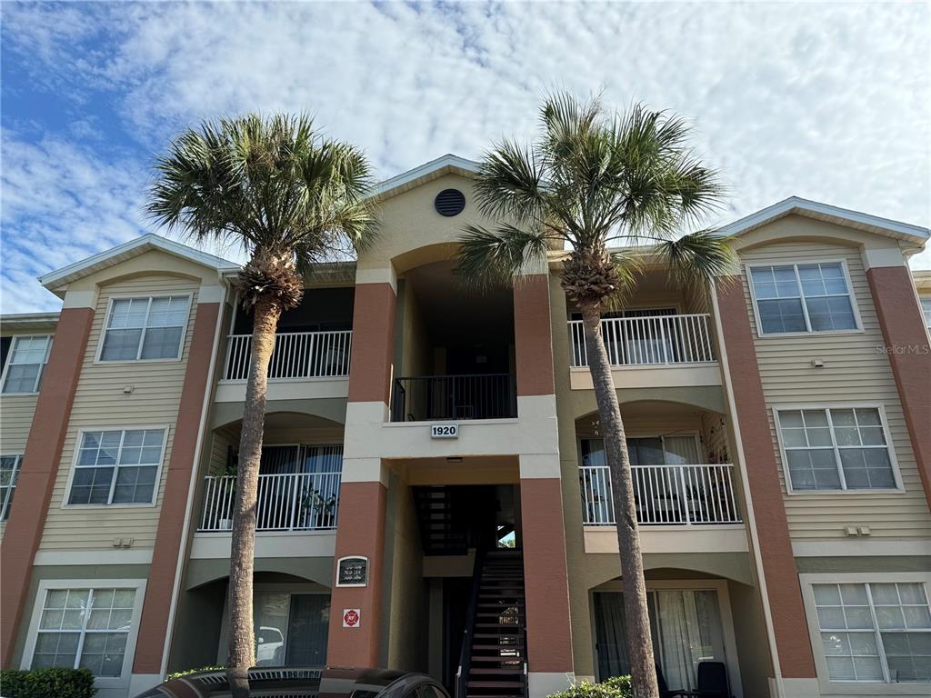 A three-story apartment building exterior features tan siding, orange accents, and two tall palm trees — 1920 SUMMER CLUB DRIVE UNIT 202, OVIEDO, FL