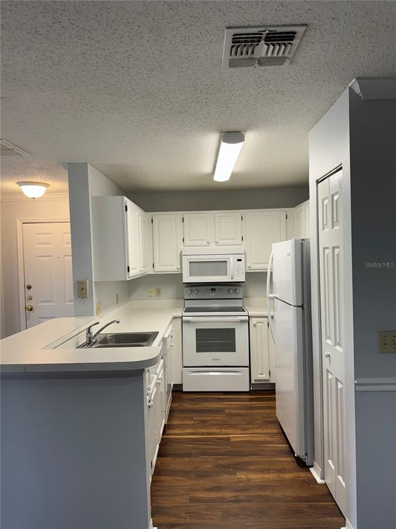 A kitchen features white cabinets, white appliances, a peninsula counter, and dark wood-look flooring — 1920 SUMMER CLUB DRIVE UNIT 202, OVIEDO, FL