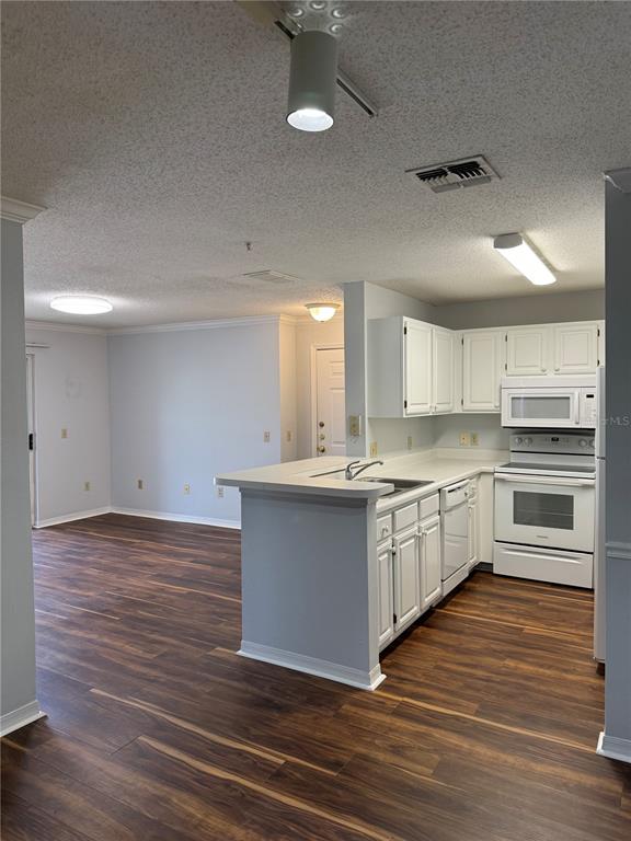 A kitchen with white cabinets and appliances opens to a living area with wood flooring — 1920 SUMMER CLUB DRIVE UNIT 202, OVIEDO, FL