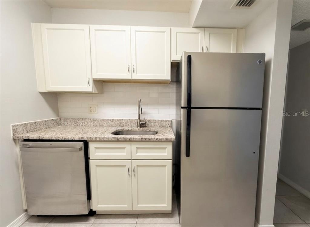 A kitchen features white cabinets, granite countertops, a stainless steel dishwasher, and a stainless refrigerator — 3244 S SEMORAN BOULEVARD UNIT 24, ORLANDO, FL