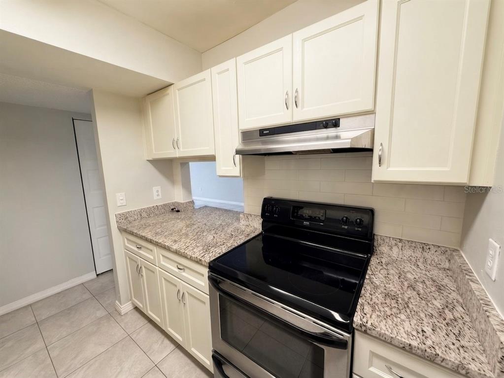 A kitchen features white cabinets, granite countertops, a stainless steel range, and light tile flooring — 3244 S SEMORAN BOULEVARD UNIT 24, ORLANDO, FL