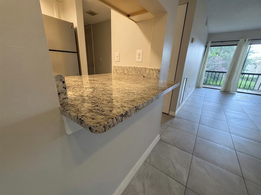 A kitchen pass-through counter with granite countertops overlooks a tiled living area with balcony access — 3244 S SEMORAN BOULEVARD UNIT 24, ORLANDO, FL
