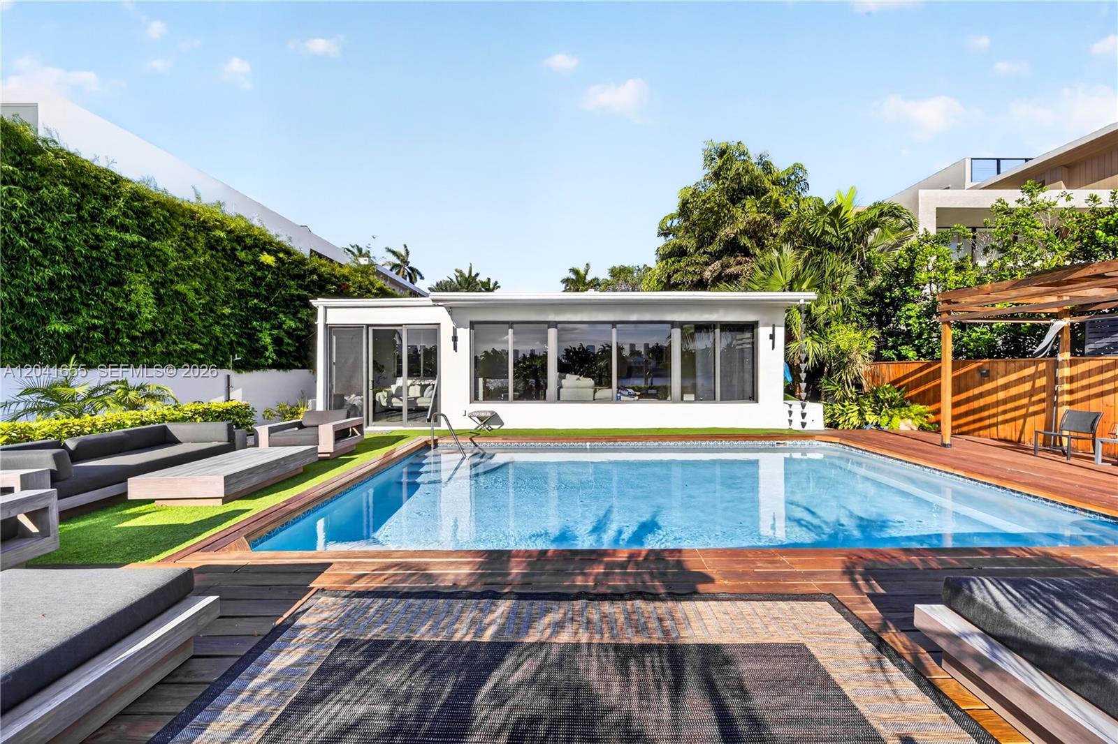 A rectangular swimming pool sits on a wooden deck in front of a modern building — 460 W Dilido Dr, Miami Beach FL 33139, MIAMI BEACH, FL