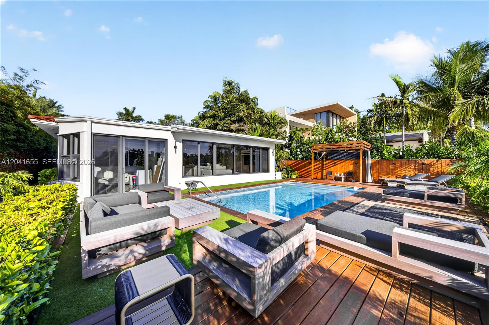 A backyard features a swimming pool, wooden decking, artificial turf, and modern outdoor lounge furniture — 460 W Dilido Dr, Miami Beach FL 33139, MIAMI BEACH, FL