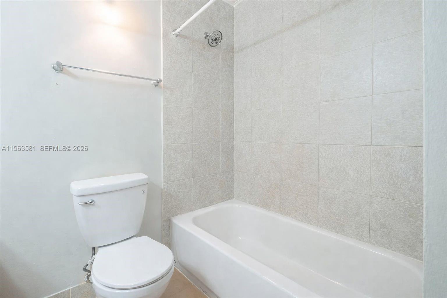 A bathroom features a white toilet next to a bathtub with light-colored tiled walls — 2075 NW 46th Ave # I201, Lauderhill FL 33313, LAUDERHILL, FL