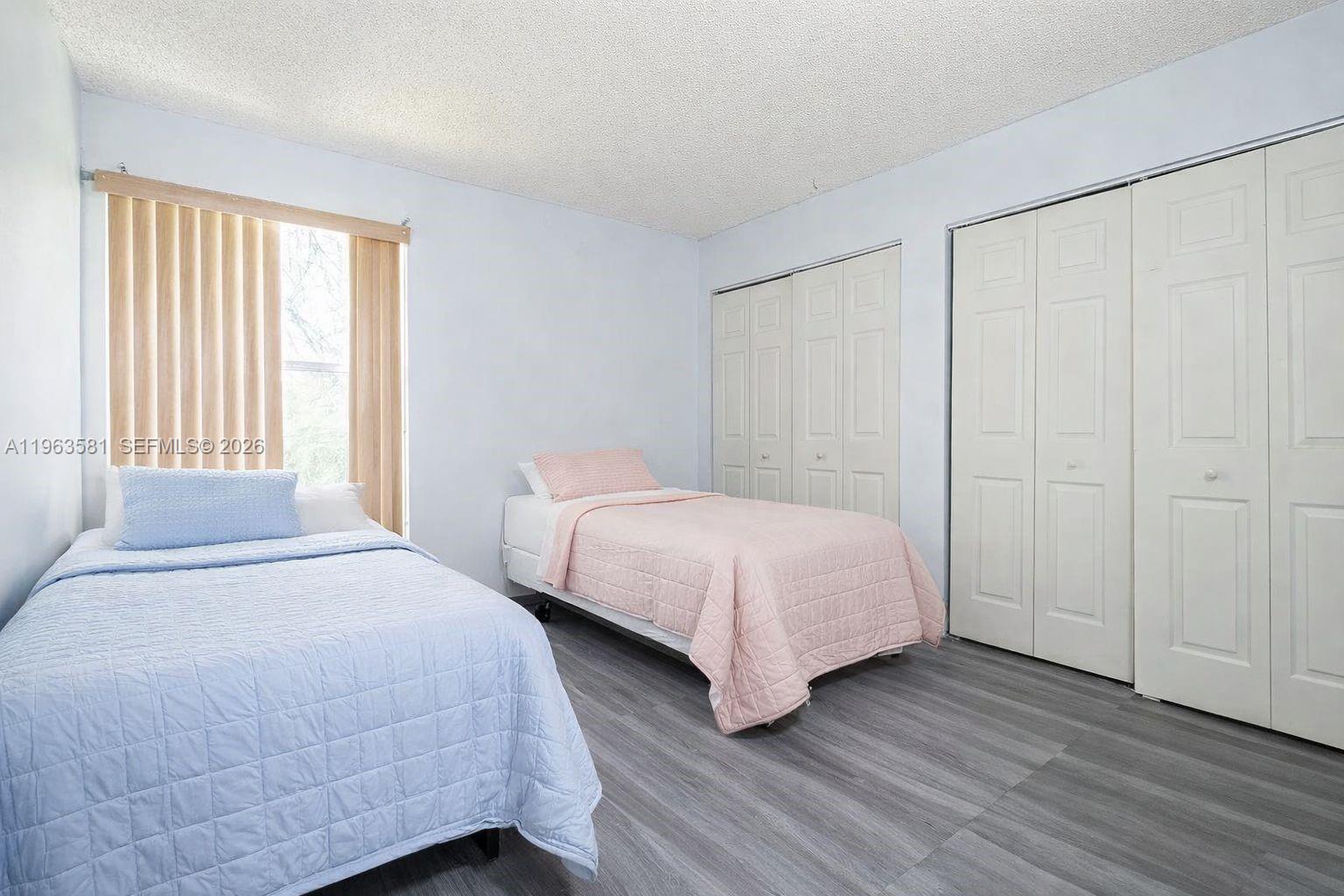 A bedroom features two twin beds, light blue walls, gray flooring, and white closet doors — 2075 NW 46th Ave # I201, Lauderhill FL 33313, LAUDERHILL, FL