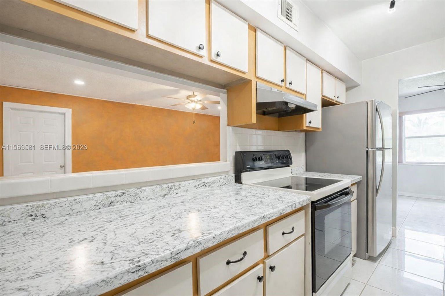 A kitchen features white cabinets, granite countertops, a stainless steel refrigerator, and a pass-through window — 2075 NW 46th Ave # I201, Lauderhill FL 33313, LAUDERHILL, FL