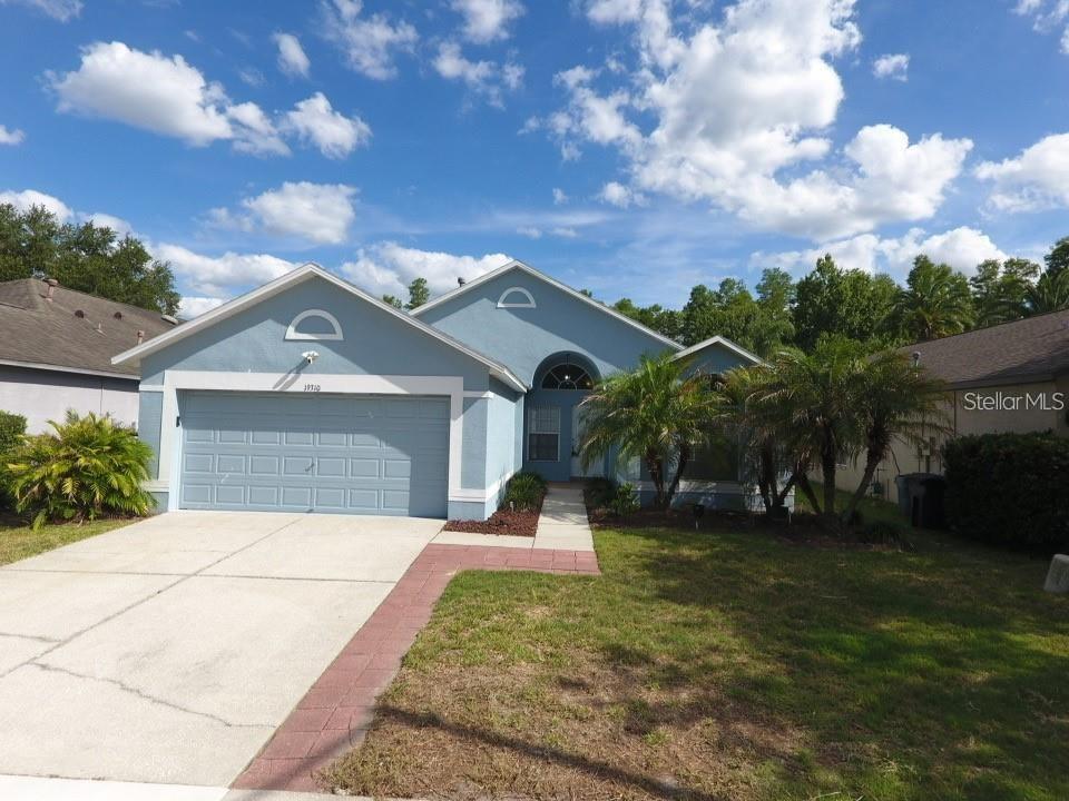 A light blue single-story house with a two-car garage and a paved walkway — 19310 WEEDON COURT, LAND O LAKES, FL
