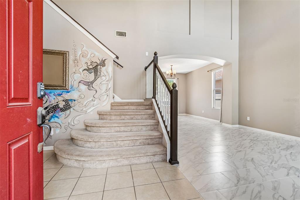 An entryway features a red front door, a carpeted staircase with a koi mural, and tile flooring — 8718 SANDY PLAINS DRIVE, RIVERVIEW, FL