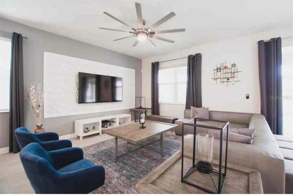 A living room features a wall-mounted television, a sectional sofa, two blue chairs, and wood-toned furniture — 9024 SOMMERSET HILLS DRIVE, DAVENPORT, FL