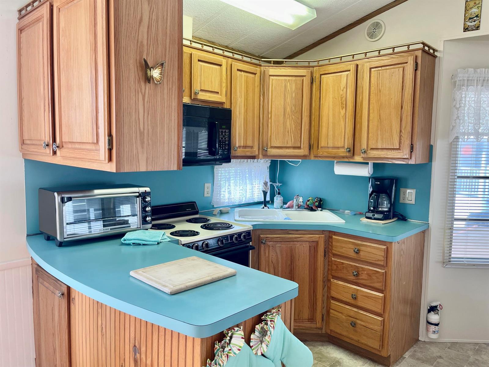 A kitchen features oak cabinets, teal countertops, a white stove, and a corner sink — 5374 SE 64th Avenue, Okeechobee FL 34974, OKEECHOBEE, FL