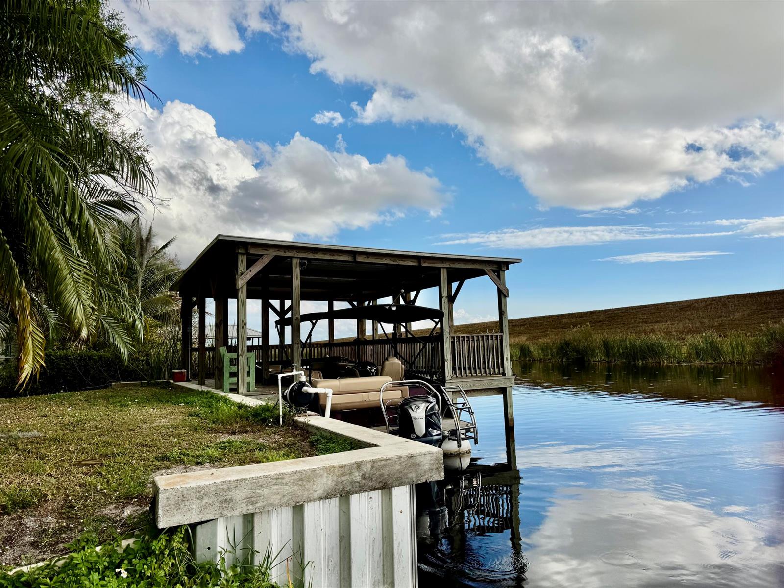 A covered wooden boat dock sits on a canal next to a grassy bank — 4390 Us Highway 441 SE, Okeechobee FL 34974, OKEECHOBEE, FL