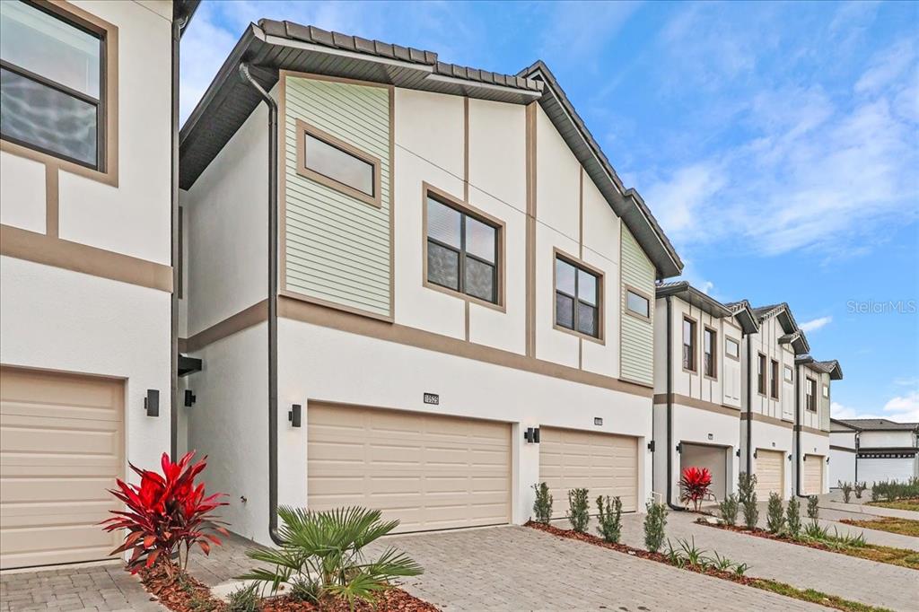 A row of modern townhomes with beige garage doors and light-colored stucco facades — 10525 EBB TIDE LANE, ORLANDO, FL