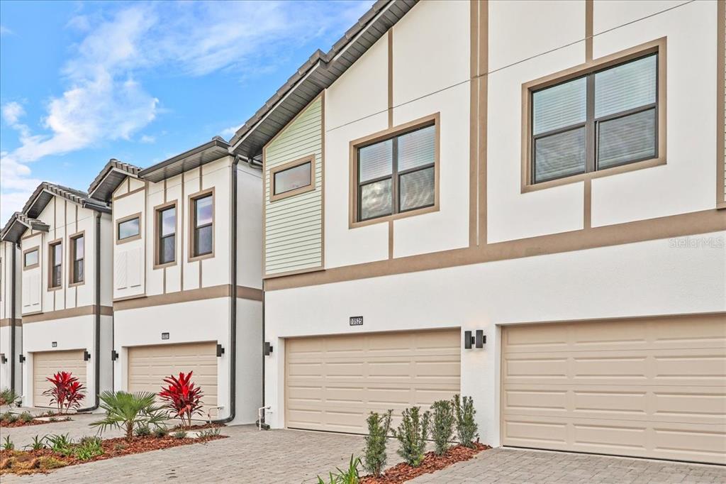 A row of modern townhomes with beige garage doors and white stucco siding under a sky — 10525 EBB TIDE LANE, ORLANDO, FL