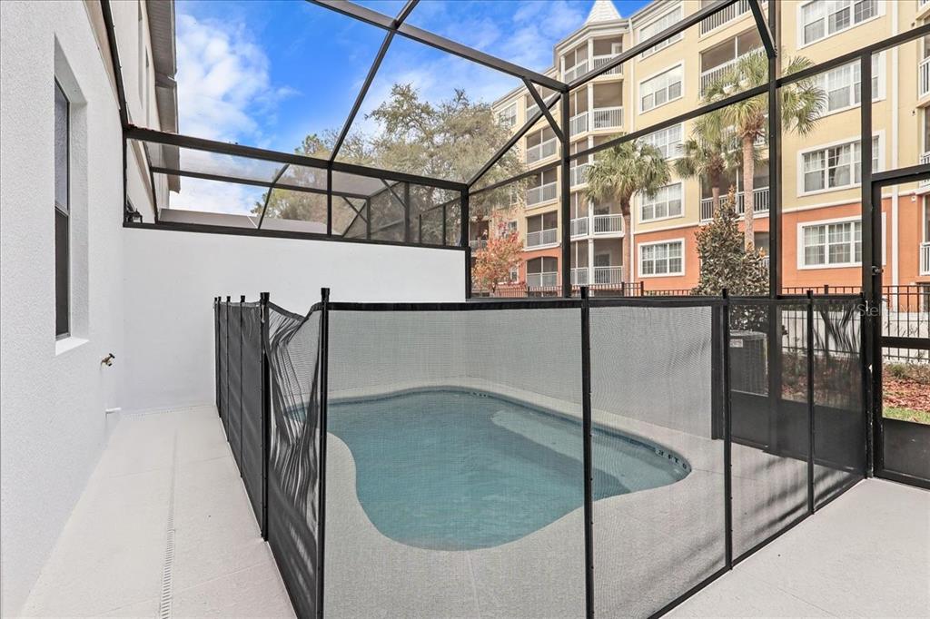 A small swimming pool is enclosed by a black safety fence inside a screened lanai — 10525 EBB TIDE LANE, ORLANDO, FL
