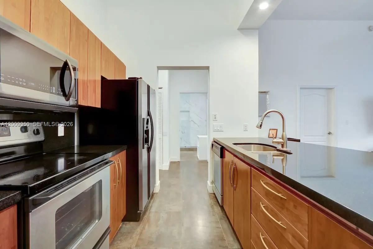 A kitchen features wood cabinets, dark countertops, stainless steel appliances, and a tiled floor — 1200 Brickell Bay Dr # 1404, Miami FL 33131, MIAMI, FL