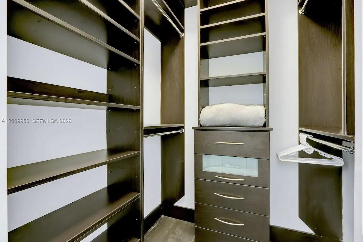 A walk-in closet features dark wood shelving, hanging rods, and a built-in drawer unit — 1200 Brickell Bay Dr # 1404, Miami FL 33131, MIAMI, FL