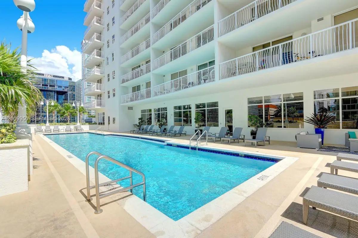 A rectangular swimming pool sits on a patio next to a multi-story white building — 1200 Brickell Bay Dr # 1404, Miami FL 33131, MIAMI, FL