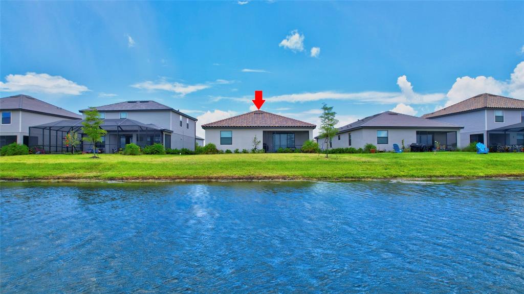 A single-story house with a tiled roof sits behind a pond under a blue sky — 5409 CORAL REEF WAY, BRADENTON, FL