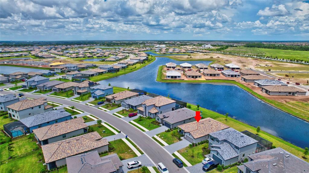 An aerial view shows a suburban neighborhood with houses surrounding a large retention pond — 5409 CORAL REEF WAY, BRADENTON, FL