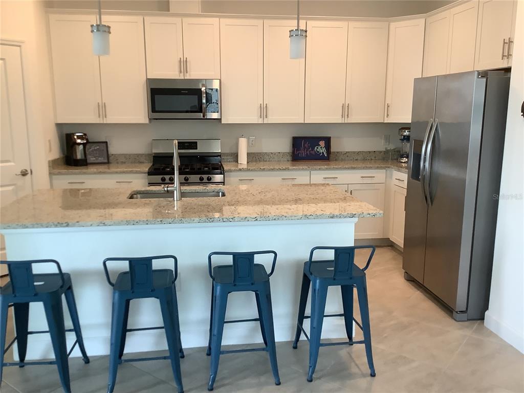 A kitchen features white cabinets, granite countertops, a stainless steel refrigerator, and four blue stools — 5409 CORAL REEF WAY, BRADENTON, FL