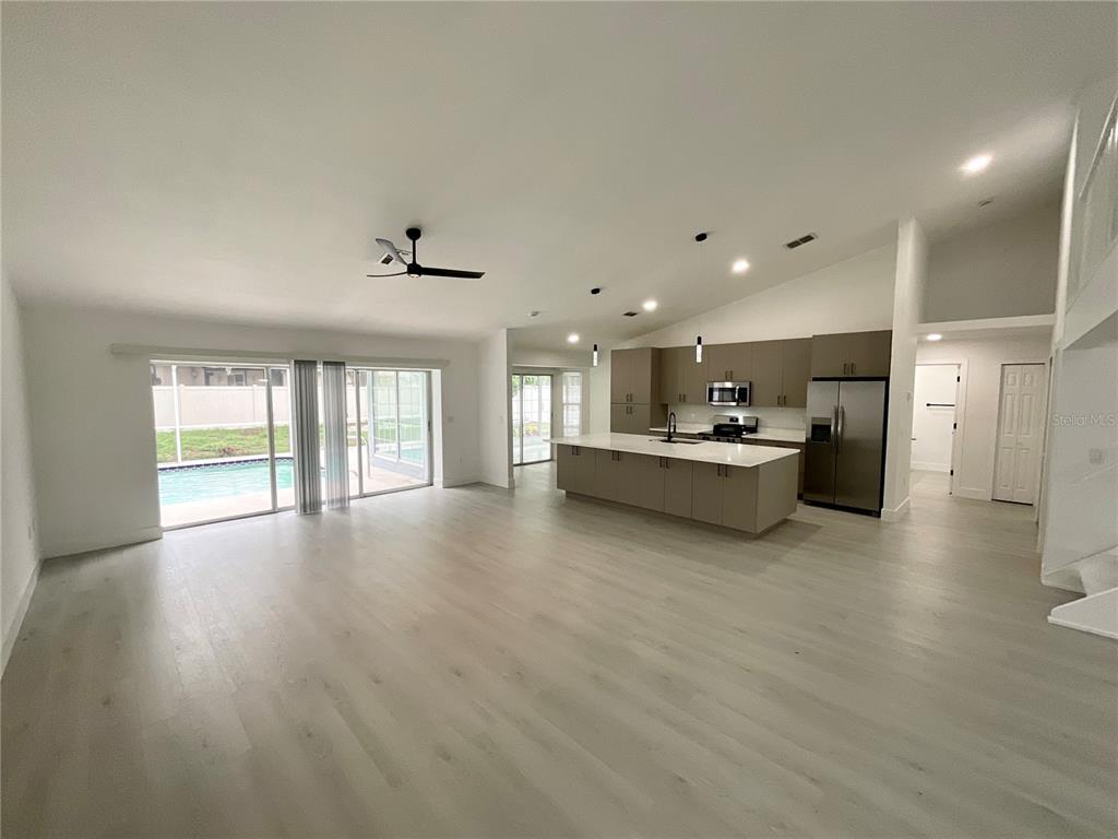 An open-concept kitchen and living area features light wood flooring, a large island, and sliding doors — 1307 BELCHER DRIVE, TARPON SPRINGS, FL