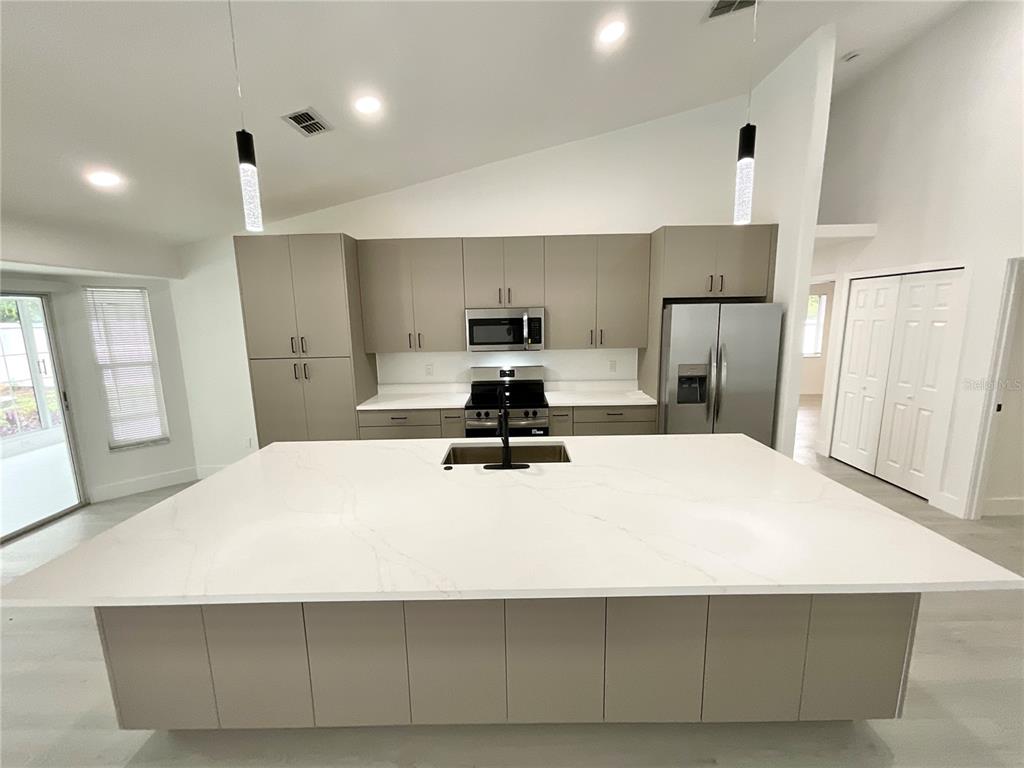 A modern kitchen features a large white island, grey cabinetry, and stainless steel appliances — 1307 BELCHER DRIVE, TARPON SPRINGS, FL