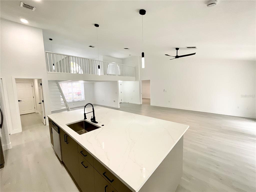 A kitchen island with a white countertop sits in an open-concept room with a loft — 1307 BELCHER DRIVE, TARPON SPRINGS, FL