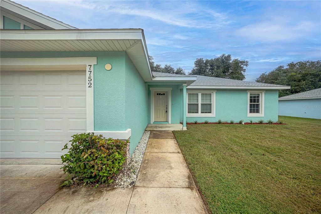 A light blue house exterior features a white garage door, front entrance, and grassy lawn — 7752 N WALTON TERRACE, CITRUS SPRINGS, FL