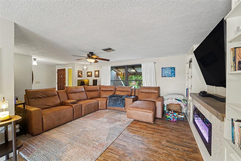 A living room features a large brown sectional sofa, a fireplace, and wood-look flooring — 5736 MELALEUCA DRIVE, HOLIDAY, FL
