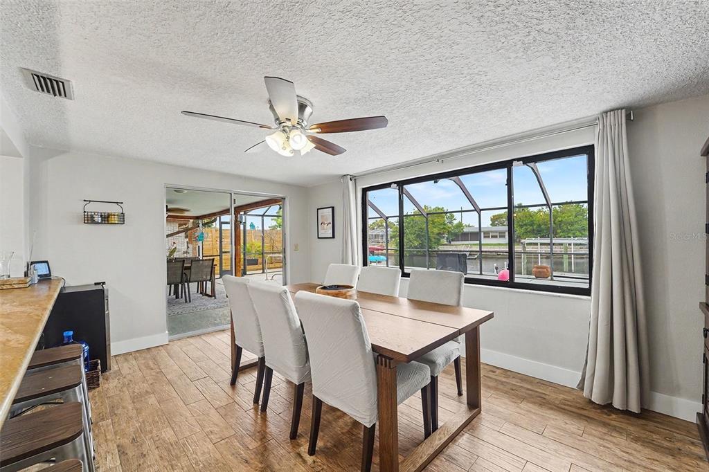 A dining room features a wooden table, white chairs, tile floors, and a waterfront view — 5736 MELALEUCA DRIVE, HOLIDAY, FL