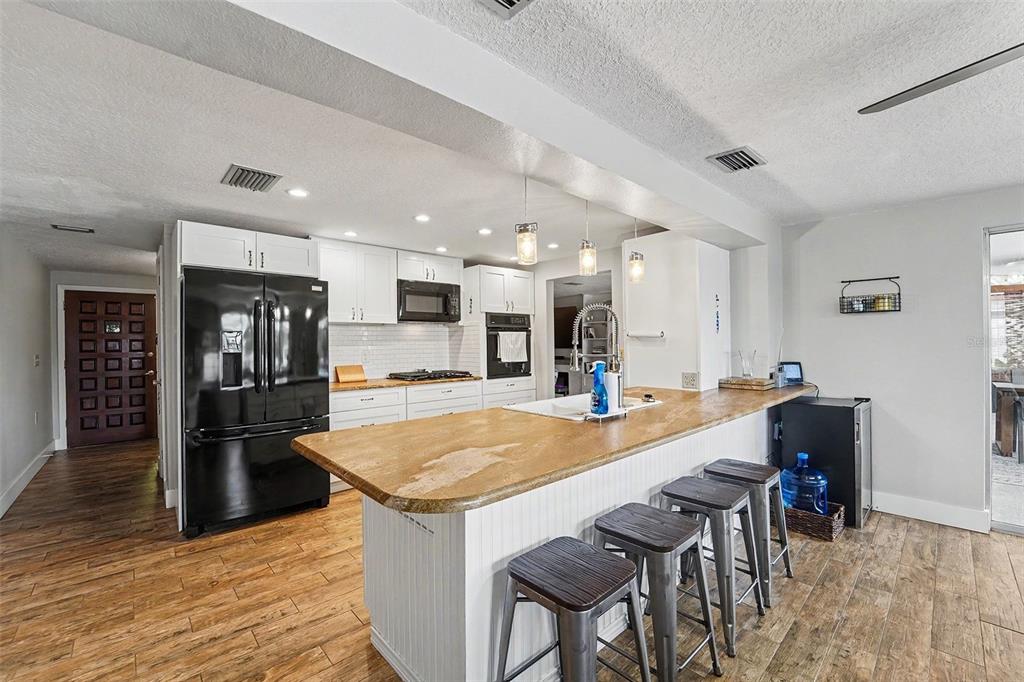A kitchen features white cabinets, a wood-topped island with bar stools, and black appliances — 5736 MELALEUCA DRIVE, HOLIDAY, FL