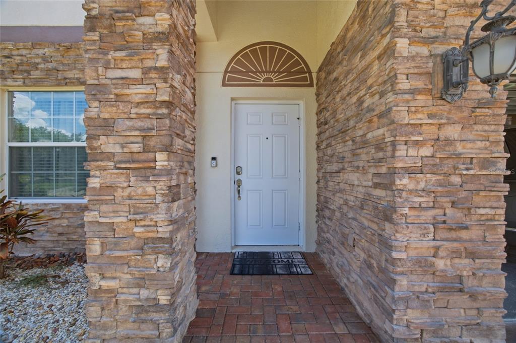 A white front door with a sunburst transom window is framed by stone-clad pillars — 12407 GILMERTON MIST LANE, RIVERVIEW, FL