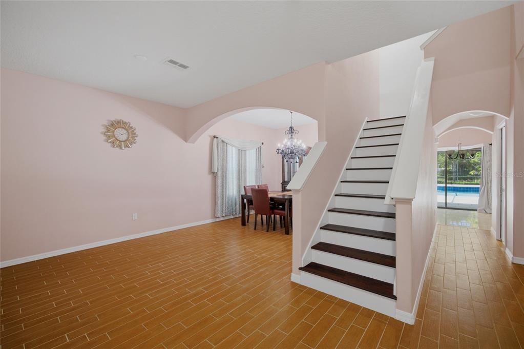 A room with light pink walls, wood-look tile flooring, and a staircase with dark treads — 12407 GILMERTON MIST LANE, RIVERVIEW, FL