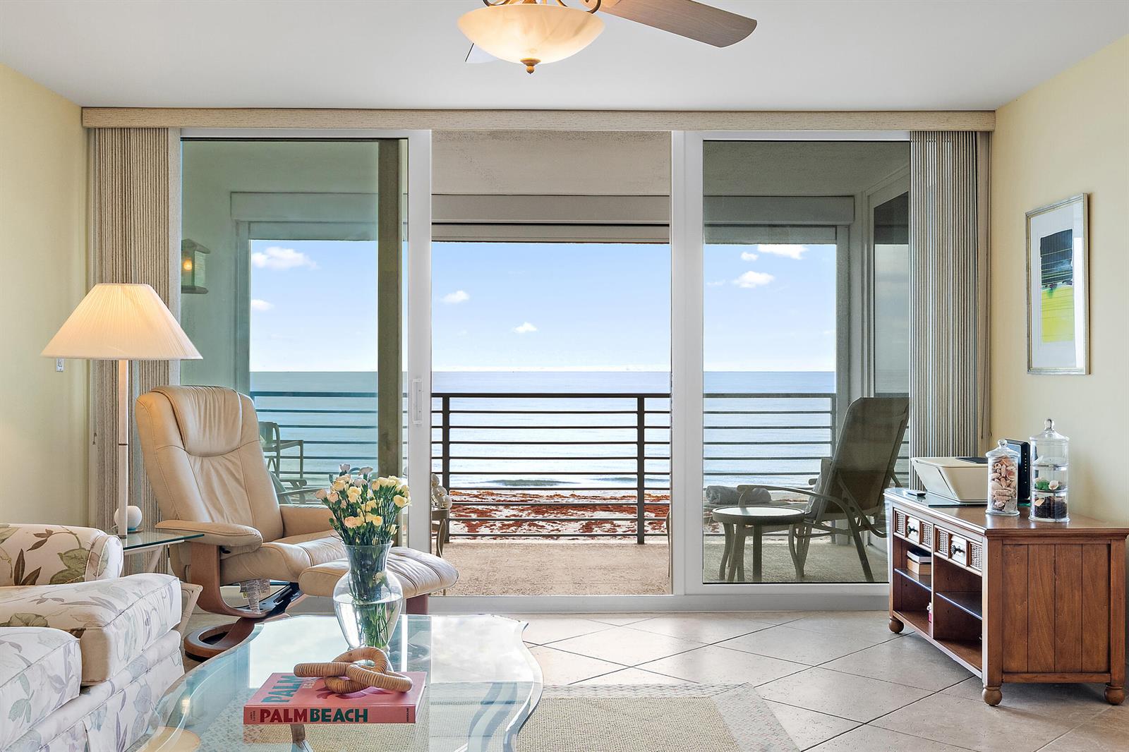 A living room with tile floors, a glass coffee table, and sliding doors overlooking the ocean — 900 Ocean Drive # 202, Juno Beach FL 33408, JUNO BEACH, FL