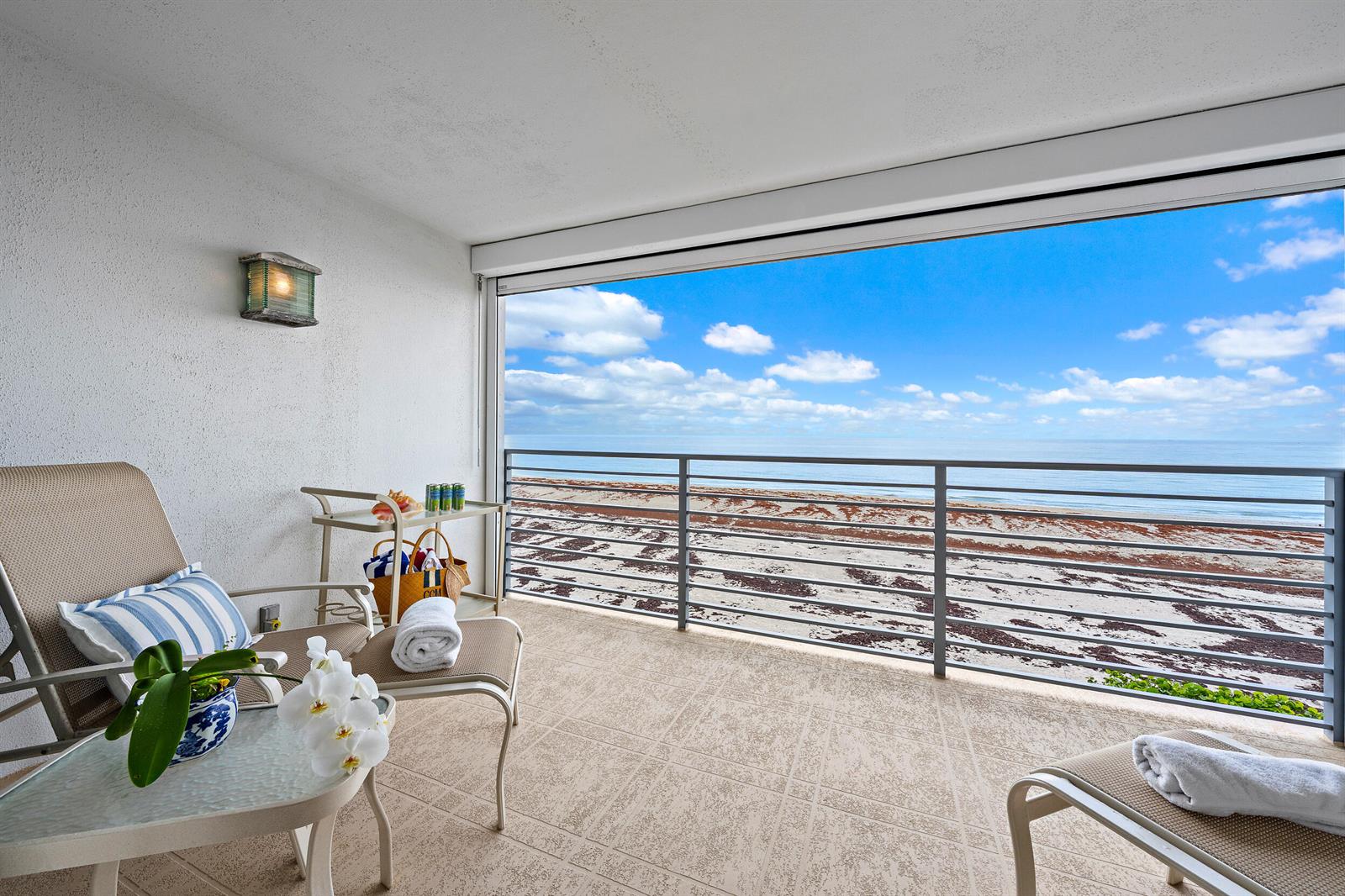 A balcony with lounge chairs and a table overlooks the beach and ocean — 900 Ocean Drive # 202, Juno Beach FL 33408, JUNO BEACH, FL