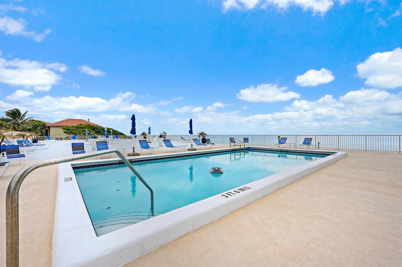 An outdoor swimming pool with lounge chairs and umbrellas overlooks the ocean — 900 Ocean Drive # 202, Juno Beach FL 33408, JUNO BEACH, FL