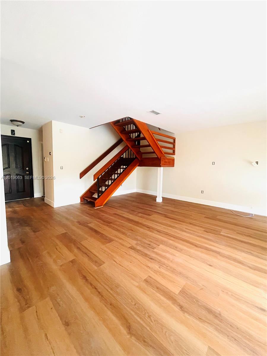 An empty room features wood-look flooring and a wooden staircase with a black metal railing — 3643 Estepona Ave # A, Doral FL 33178, DORAL, FL