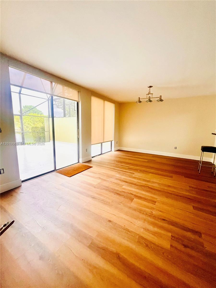 An empty room features wood-look flooring, a modern chandelier, and large sliding glass doors — 3643 Estepona Ave # A, Doral FL 33178, DORAL, FL